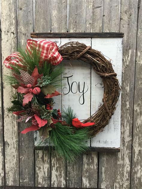 A Christmas Wreath On Top Of A Wooden Sign With The Word Joy Written In It