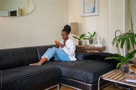 Black Girl Sitting With Phone On The Couch At Home By Stocksy
