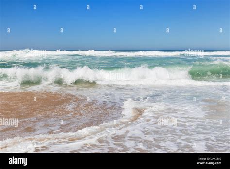 Low Angle Frontal View Of Small Foamy Ocean Waves Crashing On A Sandy