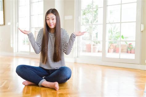 Beautiful Asian Woman Sitting Barefoot On The Floor At Home Clueless And Confused Expression
