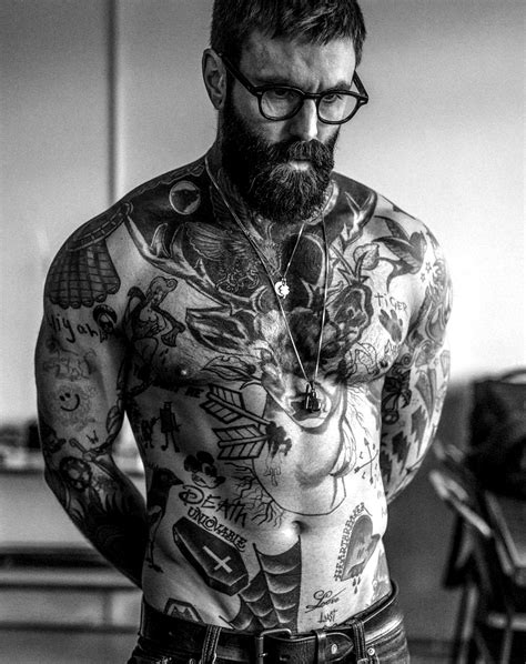 A Man With Tattoos On His Chest And Arms Is Looking At The Camera While Wearing Glasses