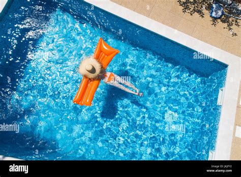Back View Of Woman Relaxing On Orange Airbed In Swimming Pool Stock