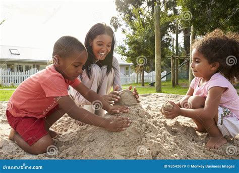 Teacher At Montessori School Playing With Children In Sand Pit Stock