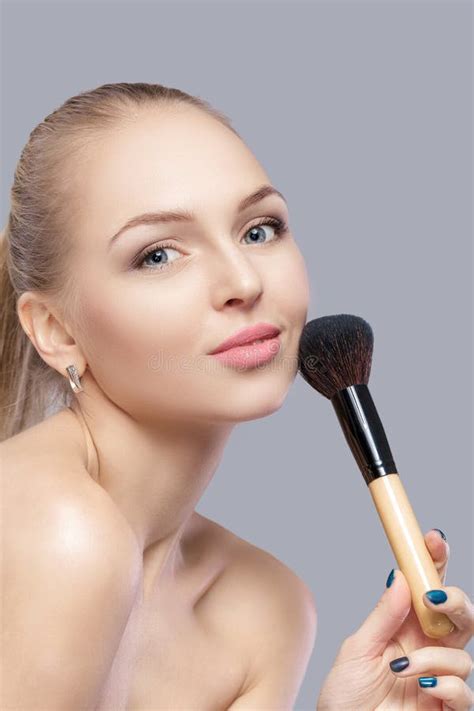 Beautiful Blond Woman Holding Makeup Brush On A Gray Background Stock