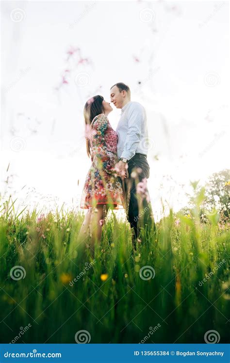 Beautiful Young Couple Gently Hugging And Kissing In Sunshine In Fresh Spring Meadow With Pink