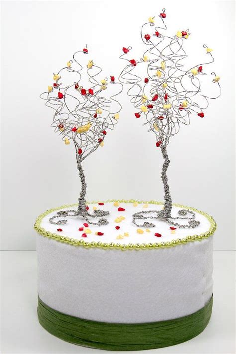 Two Wire Trees Sitting On Top Of A White Cake Covered In Red And Yellow