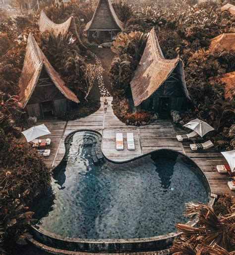 An Aerial View Of A Resort Pool Surrounded By Greenery And Thatched Roof Huts