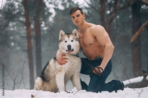 Young Bodybuilder With Bare Torso Embraces Dog Malamute At Walk In