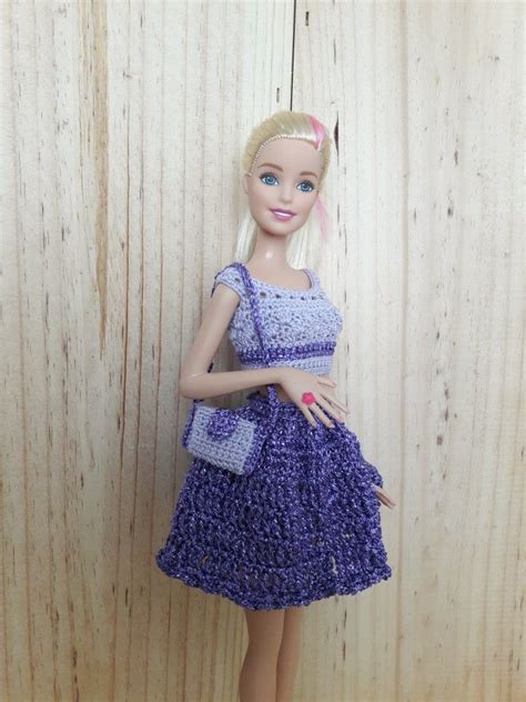 A Doll Is Wearing A Purple Dress And Holding A Handbag In Front Of A