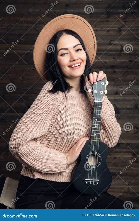 Young Brunette Women Play Ukulele Guitar In Studio On Wooden Background