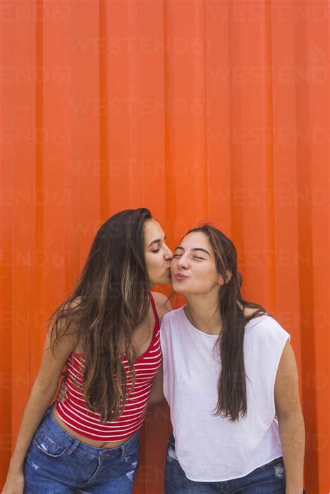 Best Friends Kissing Against Orange Wall Stock Photo