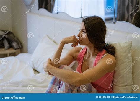 Upset Girl Sitting In Bed In Bedroom Hugging Her Knees Lost In Thought