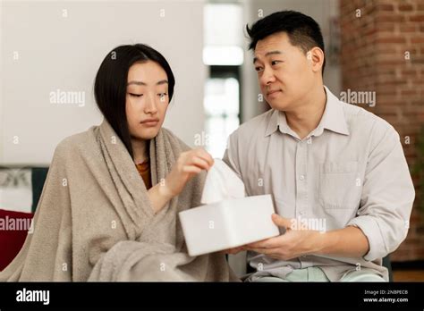 Loving Korean Middle Aged Husband Taking Care Of Sick Young Wife Sitting On Sofa Man Giving