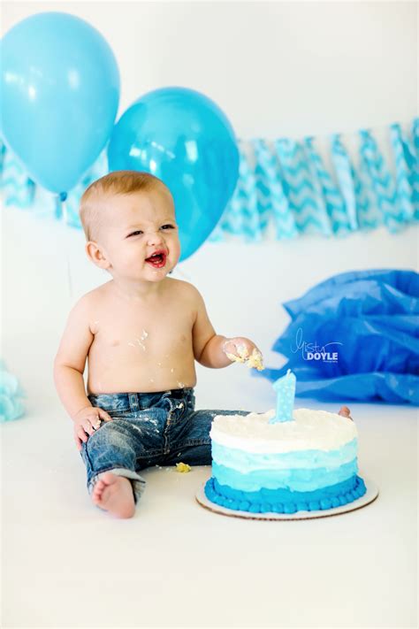 Boy blowing out candles on a birthday cake against blue background. first birthday smash cake baby boy in jeans with blue ...