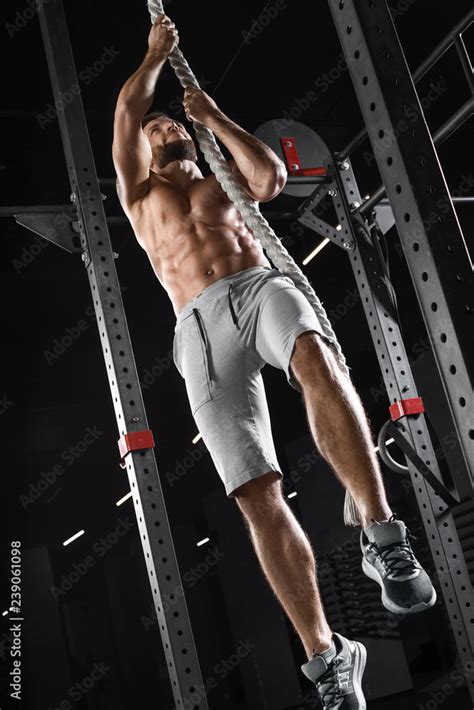 Crossfit Athlete Climbing Up The Rope In The Gym Muscular Man Doing Exercise Naked Torso Abs