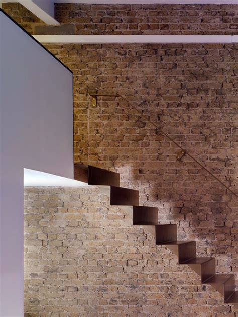 A Folded Steel Staircase Runs Alongside An Exposed Brick Wall To