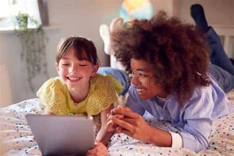 Girl And Boy In Bedroom Lying On Bed Using Digital Tablet Together