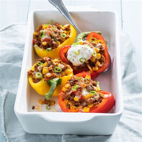Three stuffed peppers in a white casserole dish with a spoon on the side