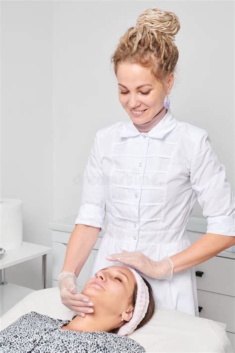 Cosmetologist In Gloves Massages Female Face Skin For Rejuvenation Procedure In Beauty Salon