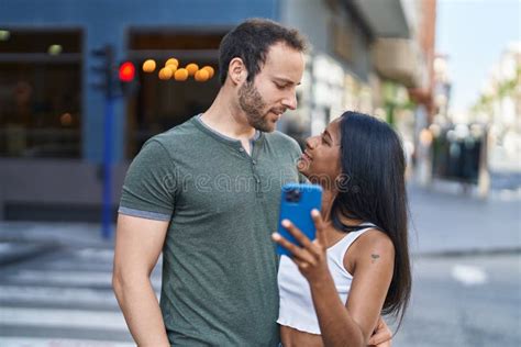 Man And Woman Interracial Couple Hugging Each Other Using Smartphone At Street Stock Image