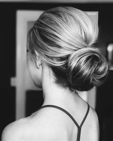 A Woman With Blonde Hair In A Low Bun Hairstyle Looking Into The Mirror
