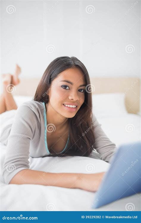 pretty girl lying on bed using her tablet smiling at camera royalty free stock image