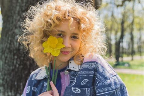 Caucasian Blonde Curly Haired Cute Girl In A Park Holding A Yellow Flower Near Her Face Outdoor