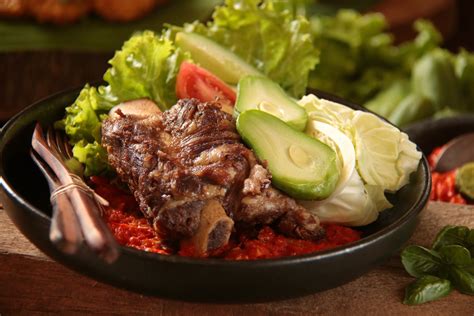 The fried beef ribs is squeezed against a mortar filled with sambal. Resep Iga Penyet Sambal Tomat