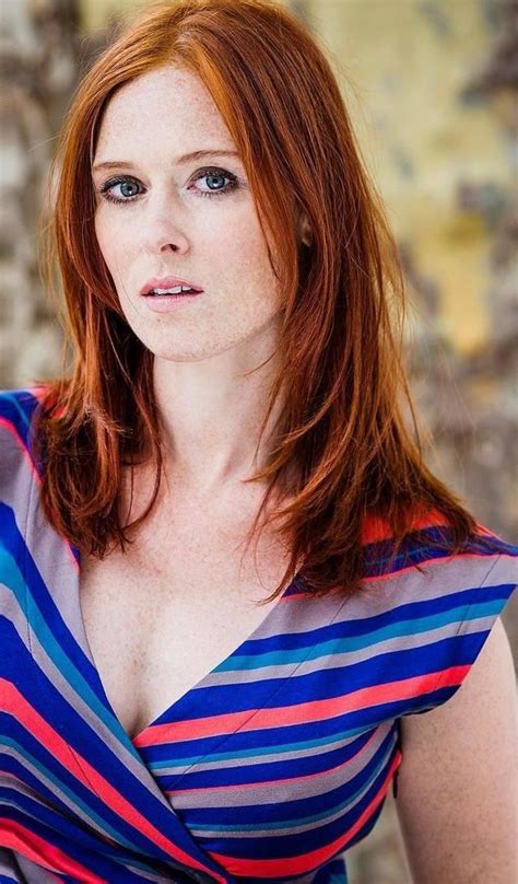a woman with red hair and blue eyes is posing for the camera while wearing a striped dress