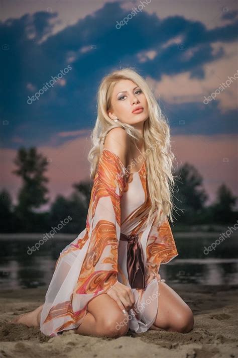 Gorgeous Blonde Woman In Transparent Blouse Posing Provocatively In Front Of A Beautiful Sunset