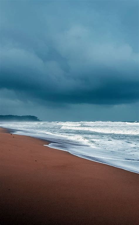 A Beach With Waves Crashing On The Shore And Dark Clouds In The Sky