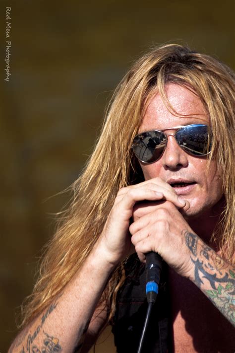 A Man With Long Hair And Sunglasses Holding A Microphone