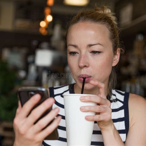Thoughtful Woman Reading News On Mobile Phone While Sipping Coffee In