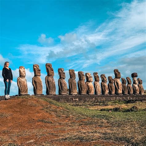 A Woman Standing In Front Of A Row Of Moai Statues On Top Of A Hill