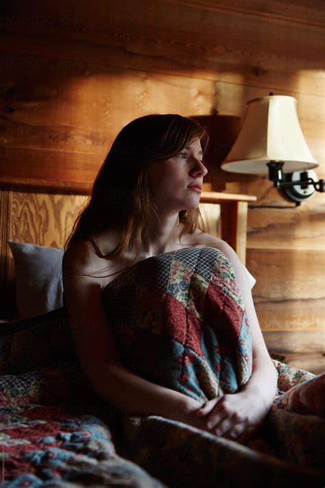 Sad Woman Sitting On Bed In Rustic Log Cabin Thinking Del Colaborador De Stocksy Trinette