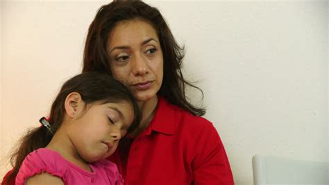 a worried hispanic single mom with little daughter waits in clinic waiting room for doctor to