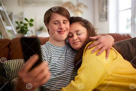 Loving Young Downs Syndrome Couple Sitting On Sofa Using Mobile Phone