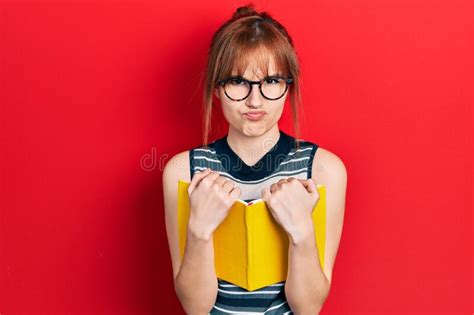 Redhead Young Woman Reading A Book Wearing Glasses Skeptic And Nervous Frowning Upset Because