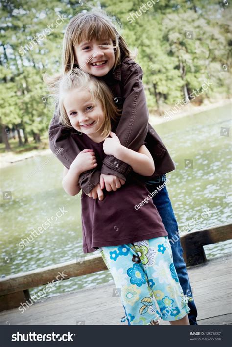 Vertically Framed Shot Of Two Cute Sisters Hugging In A Park Stock