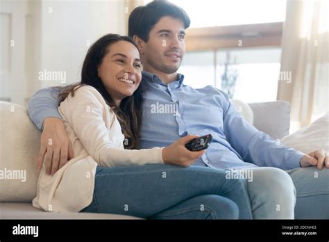 Happy Young Spouses Cuddling On Couch At Home Watching Tv Stock Photo