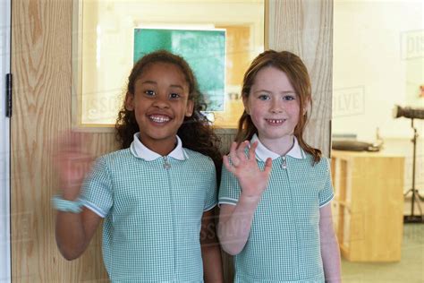 Portrait Of Two Schoolgirls Waving In Primary School Stock Photo