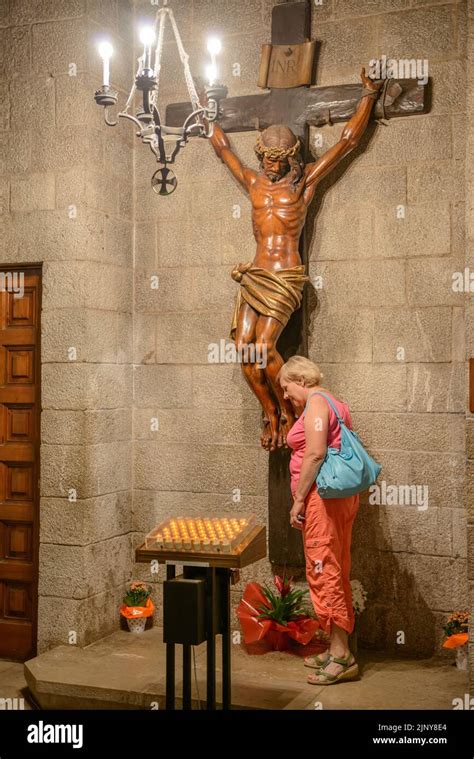 Elderly Woman Is Standing Under A Large Wooden Sculpture Of The Crucified Christ In The Interior