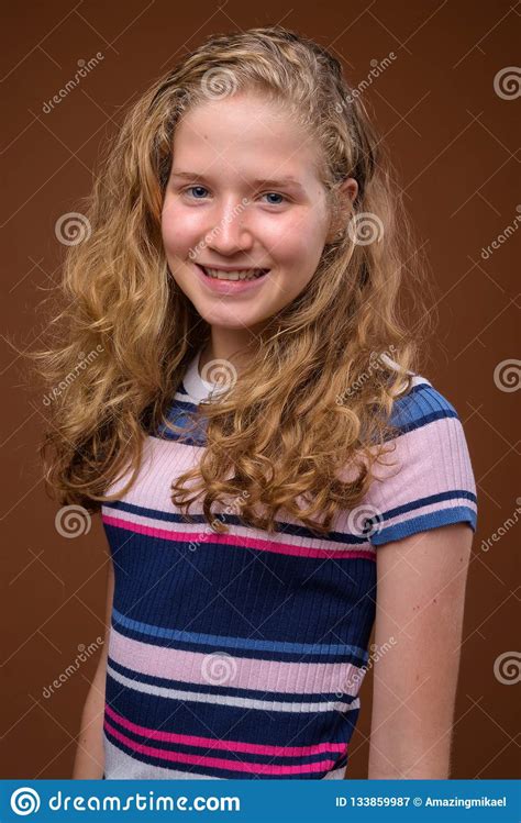 Young Beautiful Blonde Teenage Girl Smiling Against Brown Background