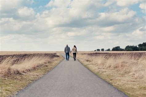 Couple Holding Hands And Walking Away On A Path In A Field On A