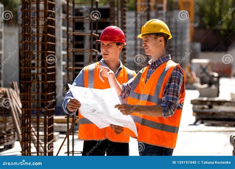 Construction Manager And Engineer Dressed In Orange Work Vests And Hard