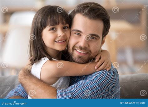Father And Daughter Embracing Sitting On Couch Looking At Camera Stock