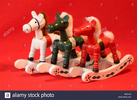 Three Wooden Rocking Horse Christmas Decorations Against A Red