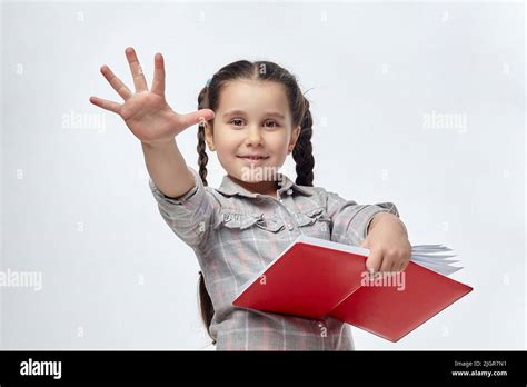 Little Black Haired Girl Holds A Red Book In Her Hands And Shows A Palm With Five Fingers