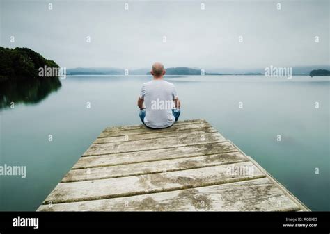 Back View Of Man Sitting On Jetty Looking At Distance Stock Photo Alamy