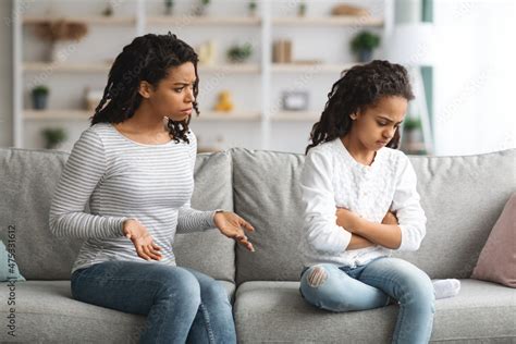 Angry Mother Scolding Daughter Sitting On Couch At Home Stock Photo